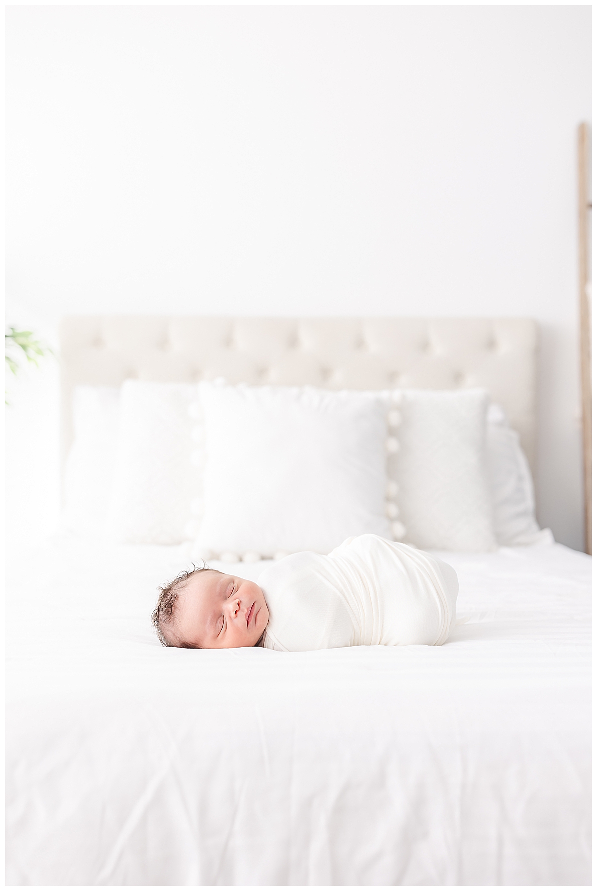 Newborn swaddled in white blanket on upholstered bed