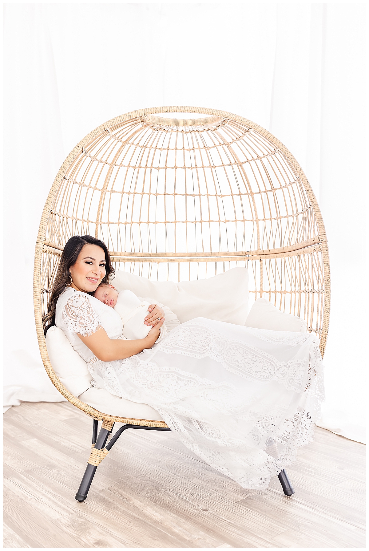 Newborn held by mom in white lace dress in whicker chair