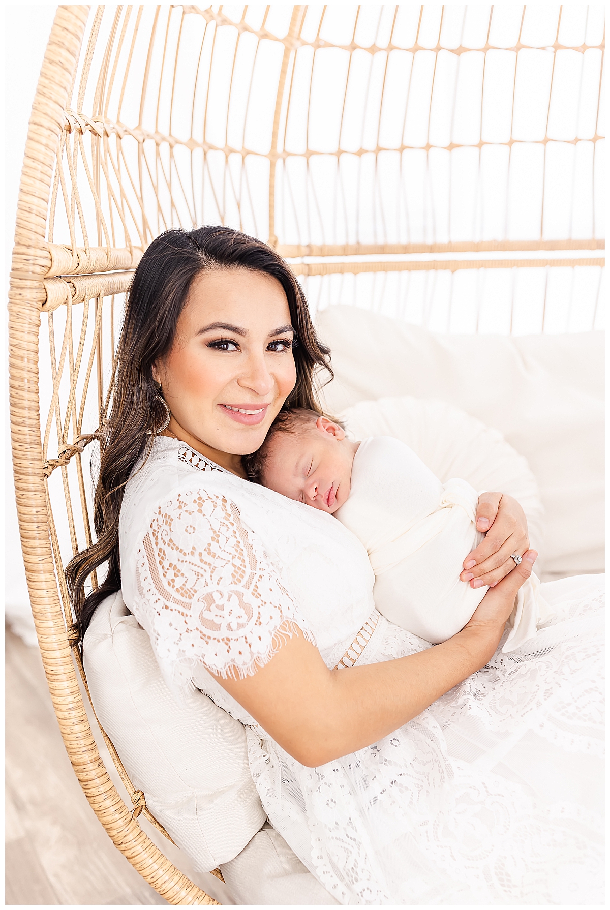 Newborn held by mom in white lace dress in whicker chair