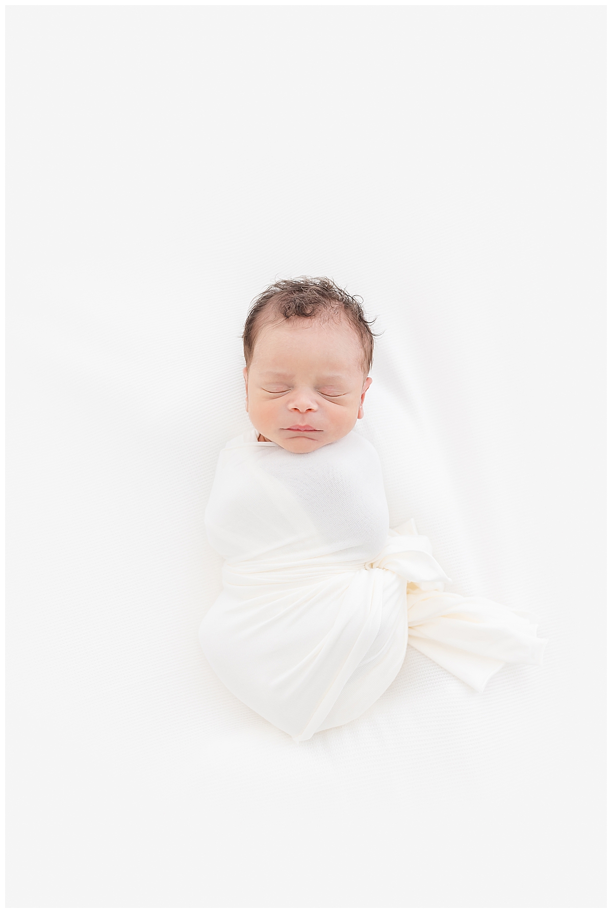 Newborn swaddled in white blanket laying on white bed