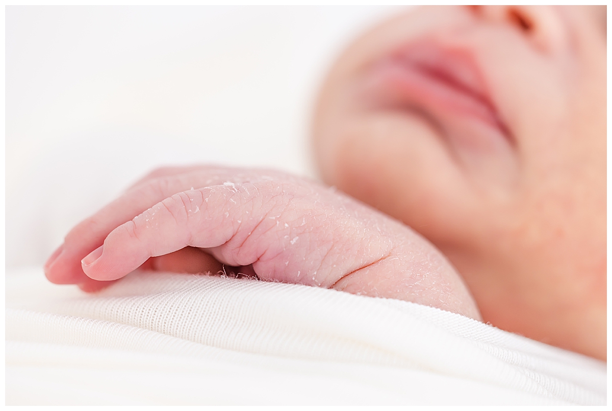 Newborn wrapped in white swaddle with close up of hand details