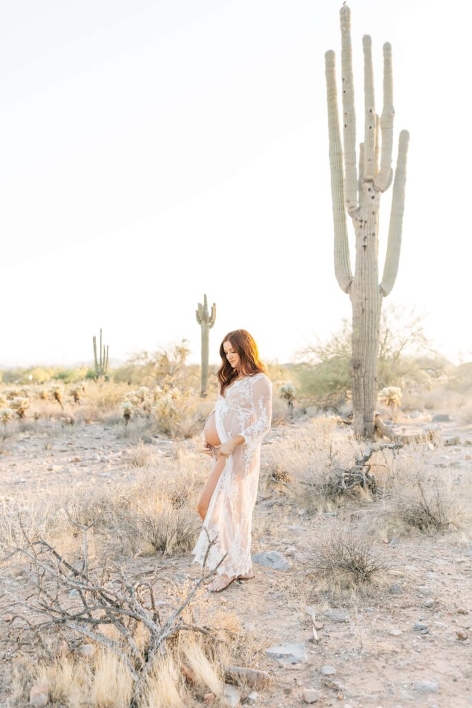 Maternity silhouette of woman in the desert wearing a white lace robe with giant saguaro in the background.