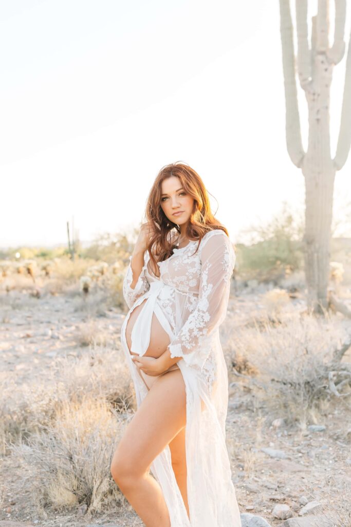 Pregnant women shares her side profile while wearing a white lace robe in the Arizona desert. 