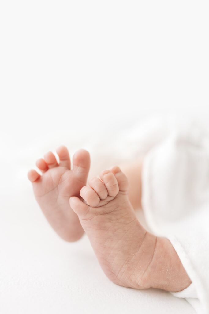 A close-up, side view of newborn feet peeking out of a white cloth. Photographed on a pure white background for this in-home newborn photography session.  .