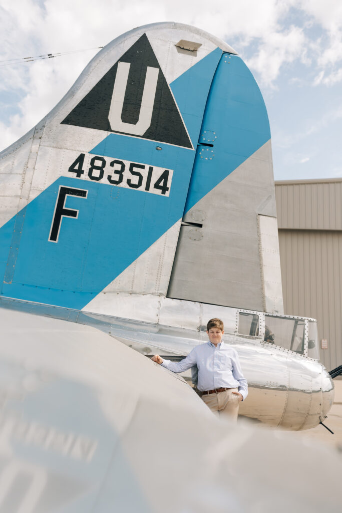 Mountain View Mesa, AZ high school senior wearing a blue button up shirt, khaki pants, and and brown belt leaning agains the tail of a U.S. Air Force plane. 