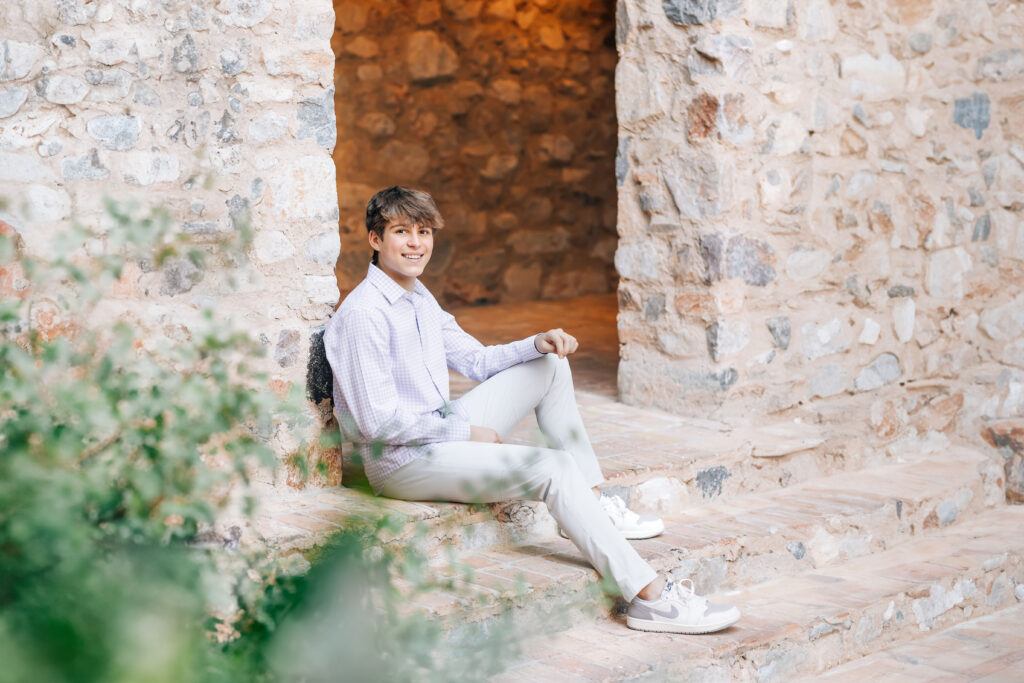 Notre Dame Prep High School Senior in Scottsdale, AZ sitting on the steps at Silverleaf Country Club wearing a purple shirt and khaki pants smiling at the camera. 