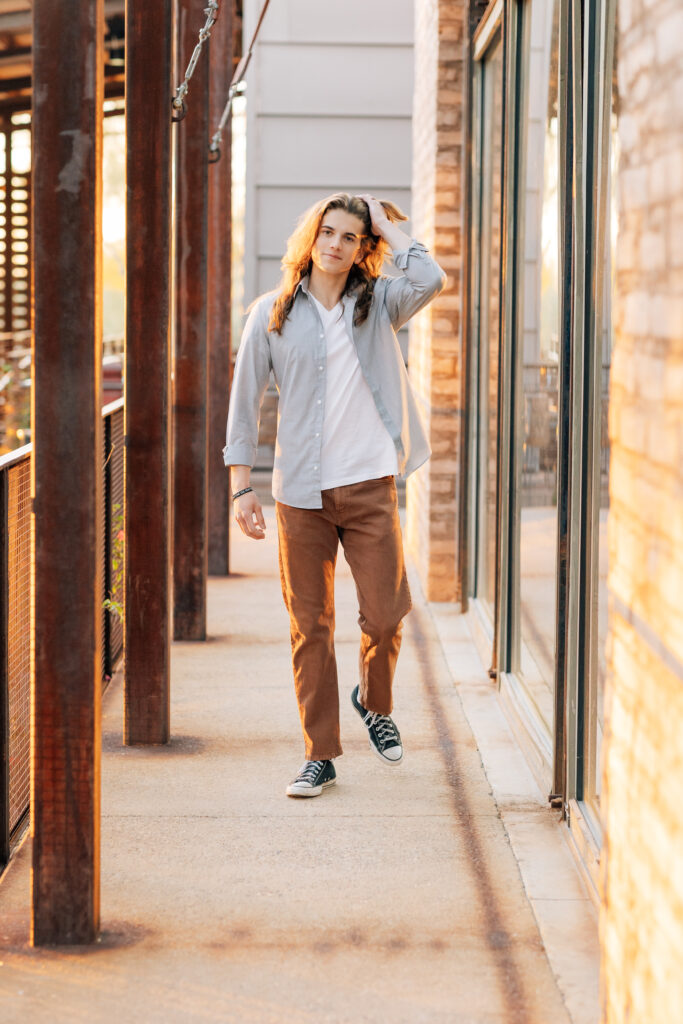 Cave Creek high School senior in brown pants, white t-shirt, and gray button up shirt walking toward the camera and running his hand through his hair. 