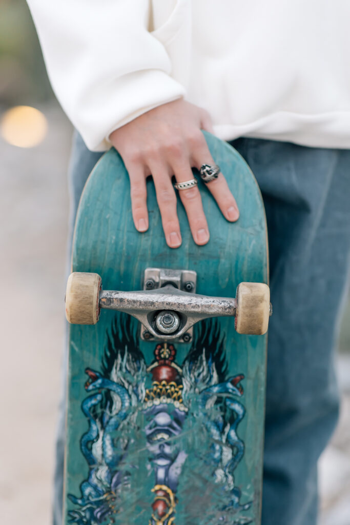 Back of skateboard being help by high school senior wearing two silver rings on his hand.