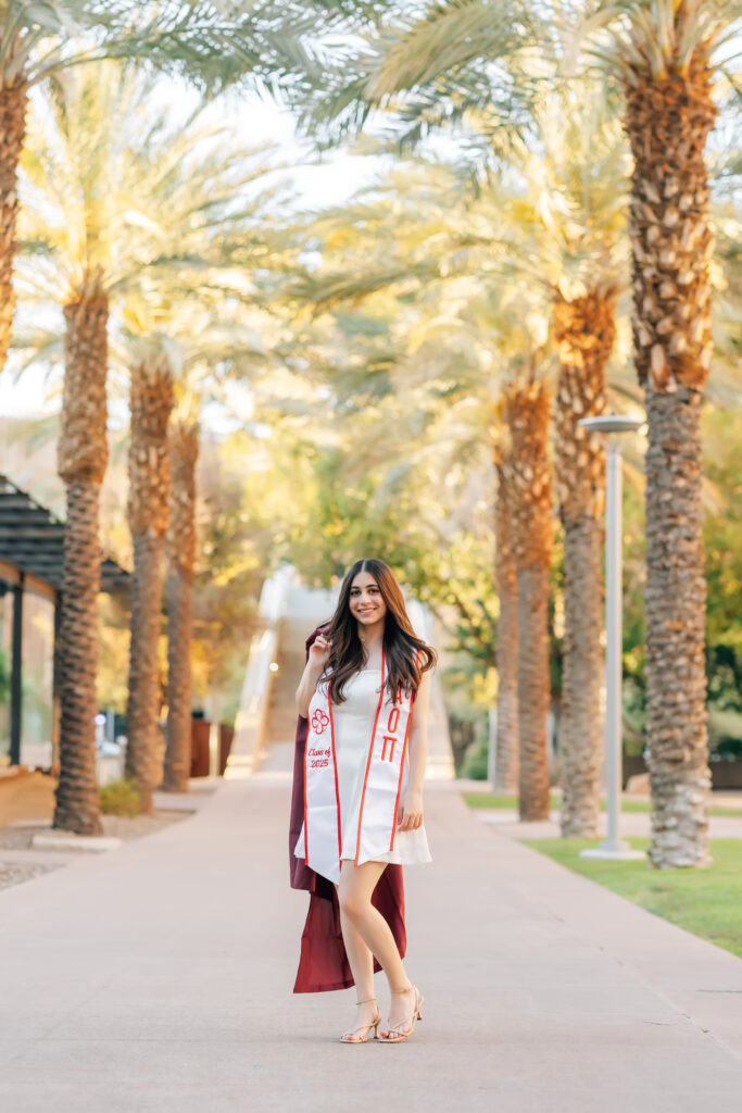 What to wear for senior pictures for girls – Tempe senior wearing a white dress and kitten heels for ASU campus senior photos with her cap and gown and sorority stole